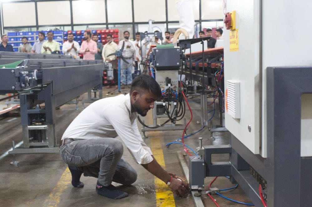 Worker adjusting machinery parts in busy factory.