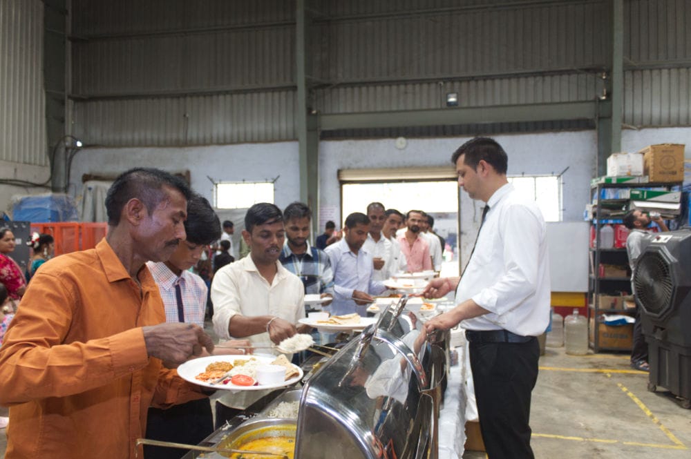 People serving food in industrial cafeteria setting.