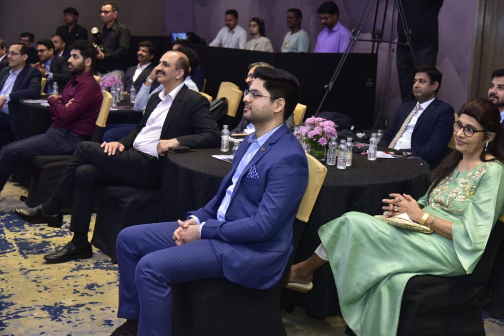Professionally dressed attendees watch a presentation at an indoor event.