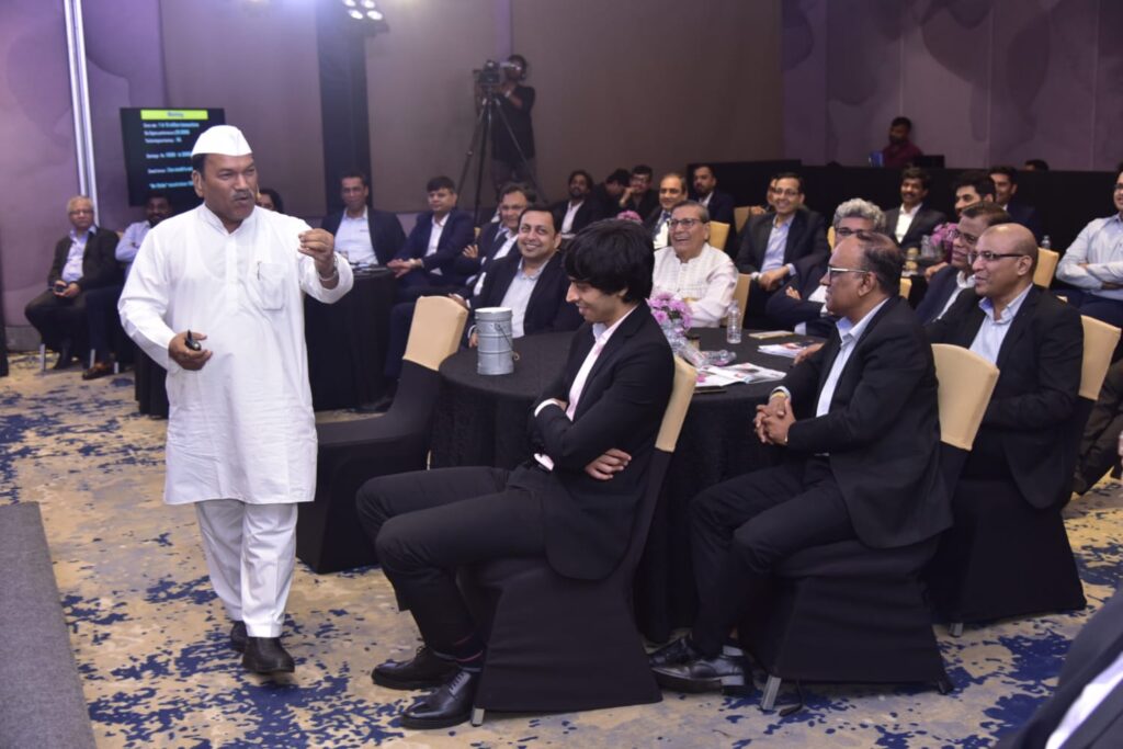 Speaker in traditional white attire addresses seated business audience