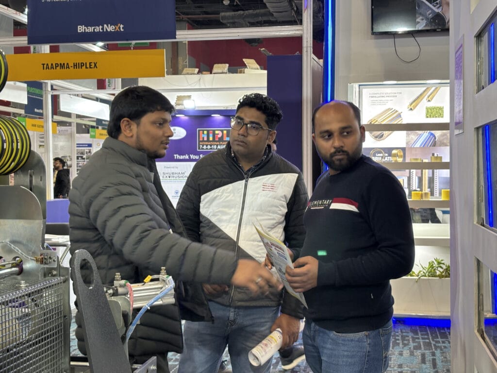 Three men discussing machinery at trade show booth