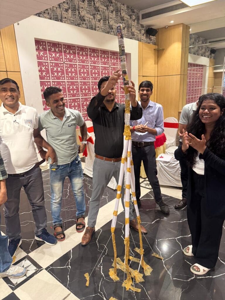 Friends celebrate beside a towering paper-tape structure indoors.
