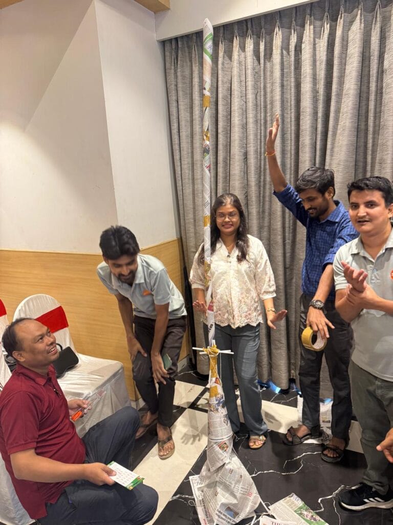Group celebrates beside a tall rolled newspaper tower.