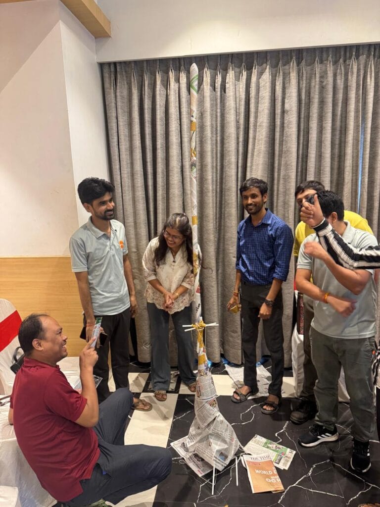 Group gathers around a newspaper tower-building activity indoors.