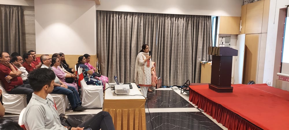 Woman speaks to seated audience at indoor presentation
